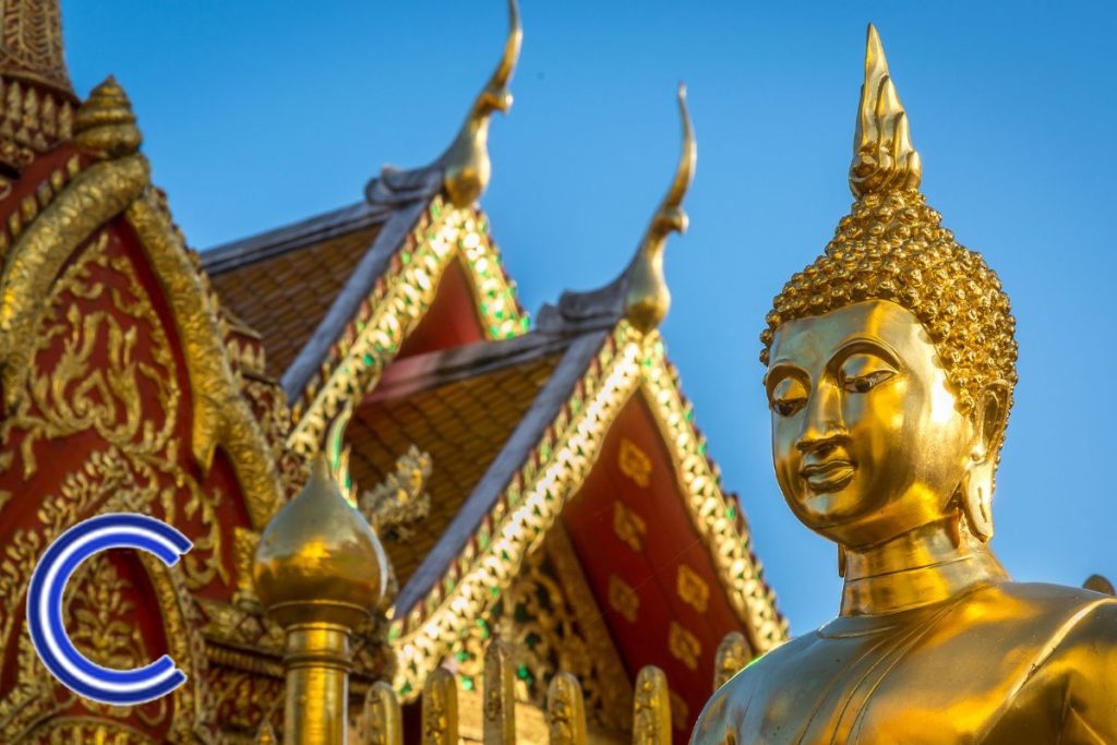 Une statue dorée d'un Bouddha devant un bâtiment orné.