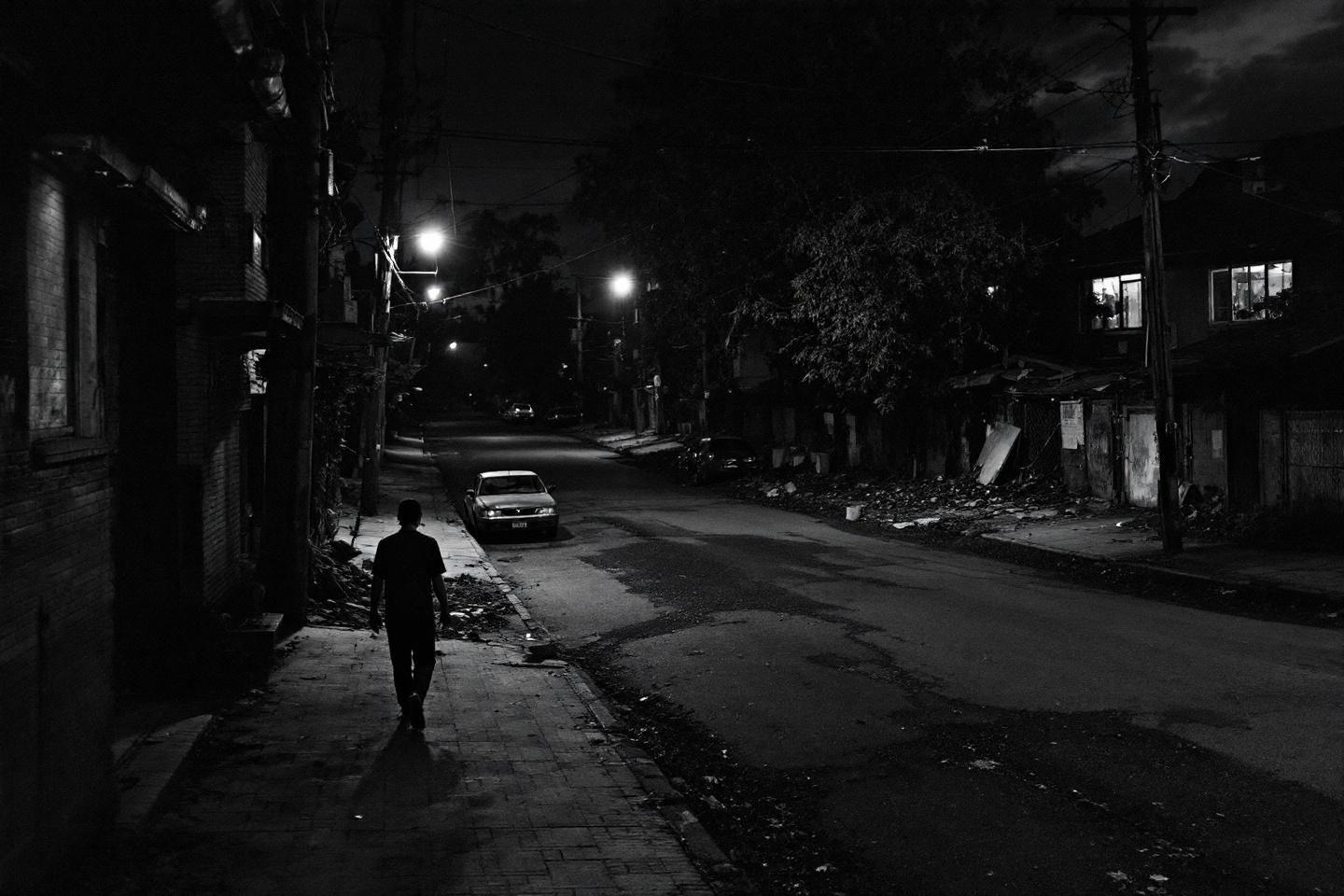 Rue sombre avec silhouette marchant pr&egrave;s d'une voiture