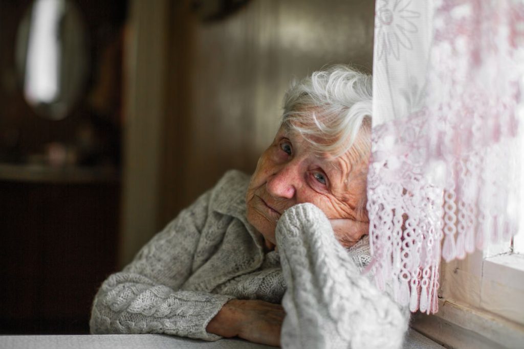 Une femme âgée appuyée sur le rebord d’une fenêtre.