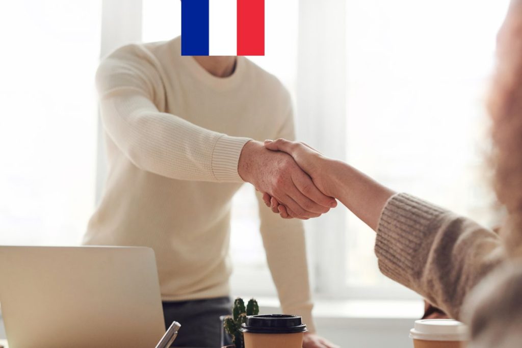 Un homme et une femme se serrent la main devant un drapeau français.