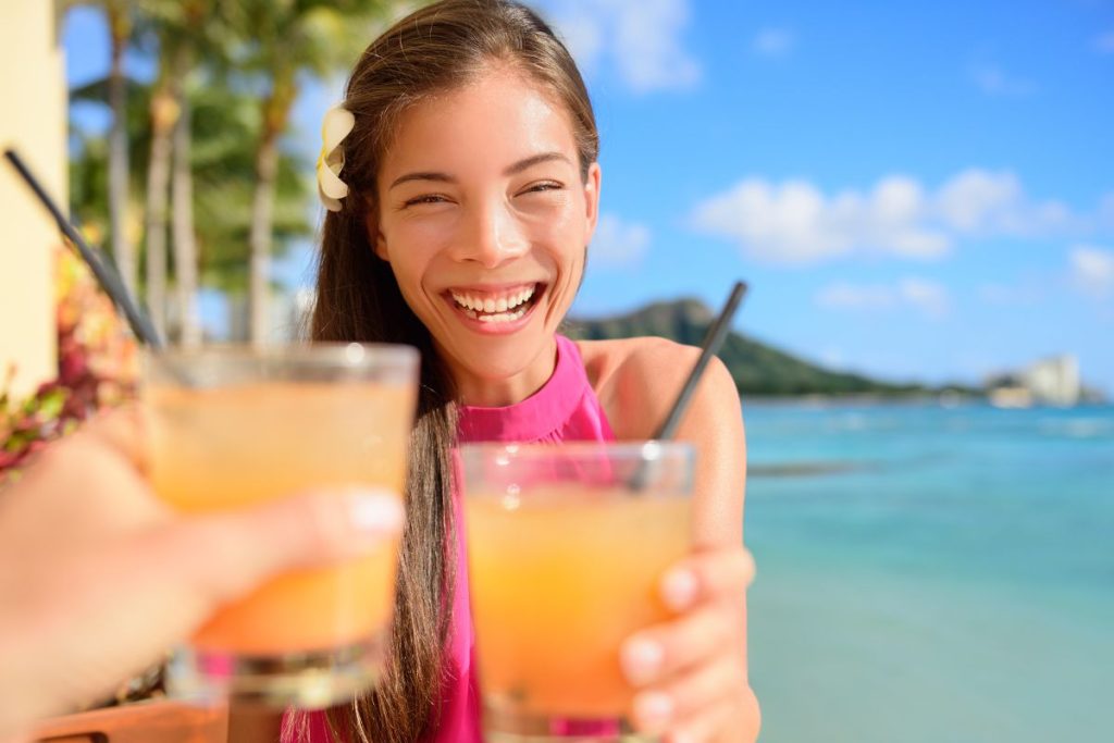 Une femme tient un verre de jus d'orange en souriant à la plage.
